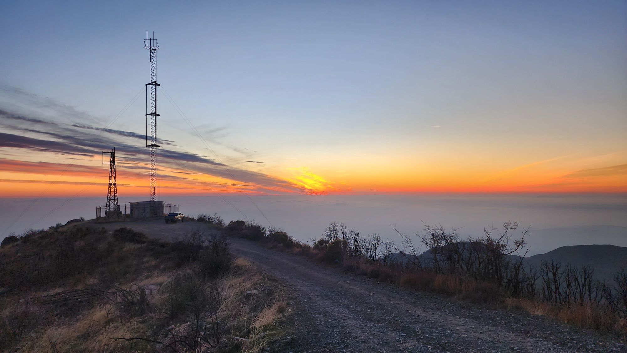 A broadcast tower on a mountain ridge at dawn, above the clouds