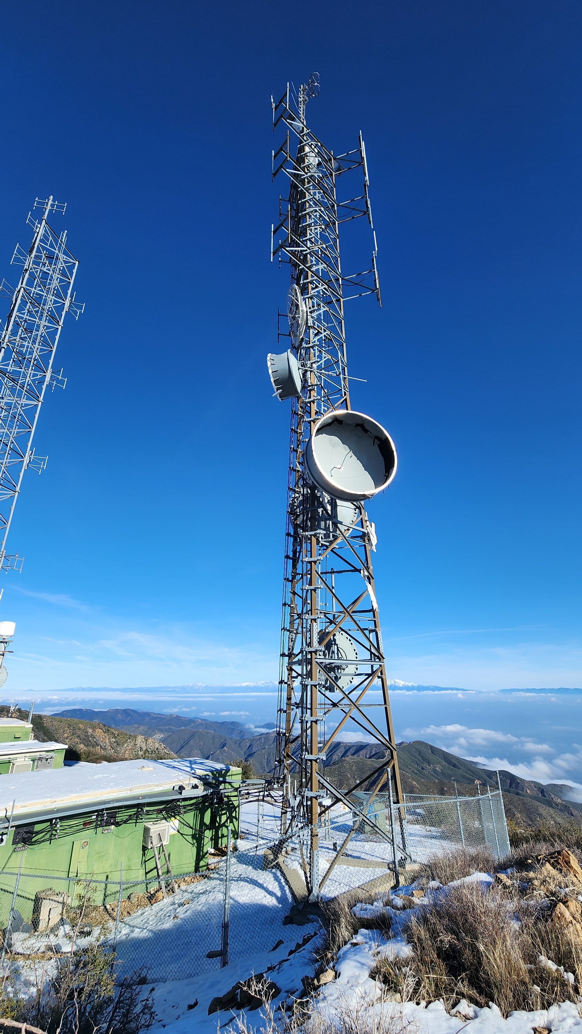 A tower with a microwave dish above snow and clouds